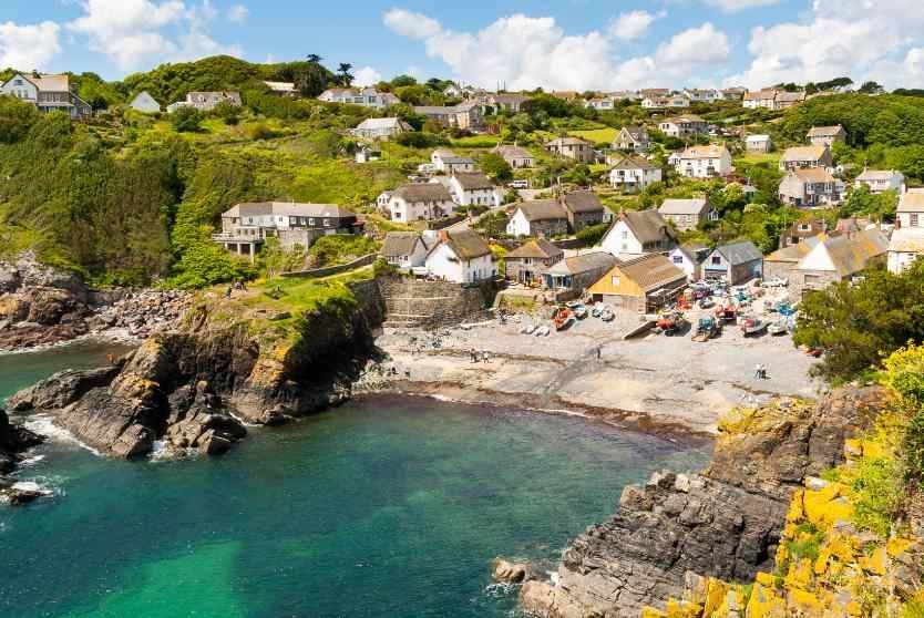 Un borgo costiero con case su una verde collina si affaccia su una caletta rocciosa con barche sulla spiaggia e acqua turchese limpida.