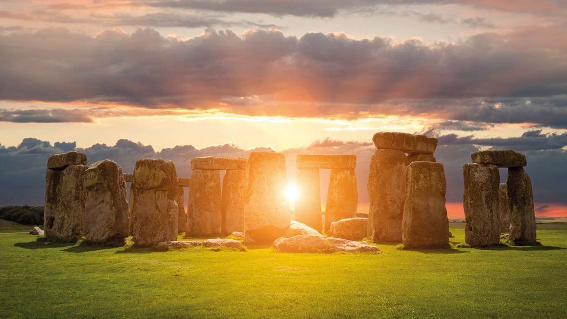L'antico cerchio di pietre di Stonehenge si erge su un campo erboso, illuminato dalla luce dorata del sole al tramonto.