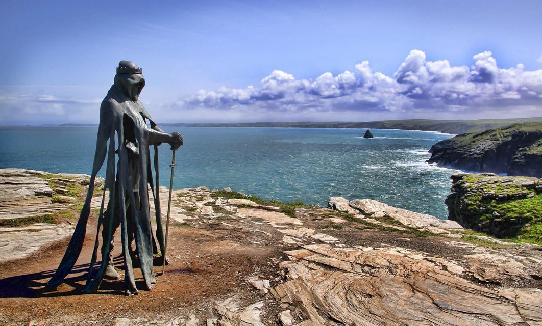 Un'alta statua in bronzo di un re che impugna una spada si erge su una scogliera rocciosa che domina un mare agitato.