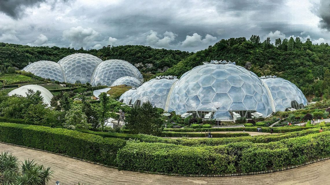 Grandi cupole geodetiche con pannelli esagonali si trovano in un rigoglioso giardino paesaggistico circondato da colline boscose sotto un cielo nuvoloso.