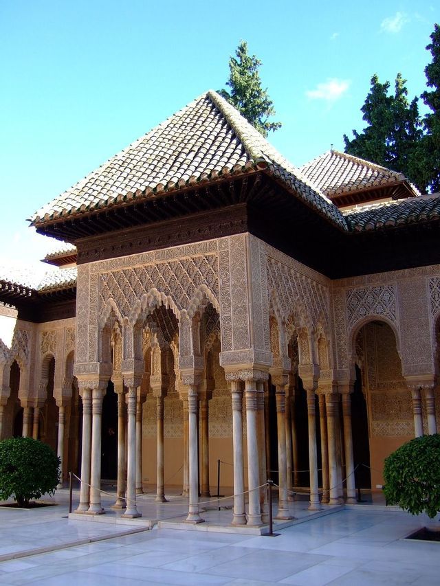 Un edificio ornamentado con arcos intrincadamente tallados y esbeltas columnas rodea un patio de mármol blanco.