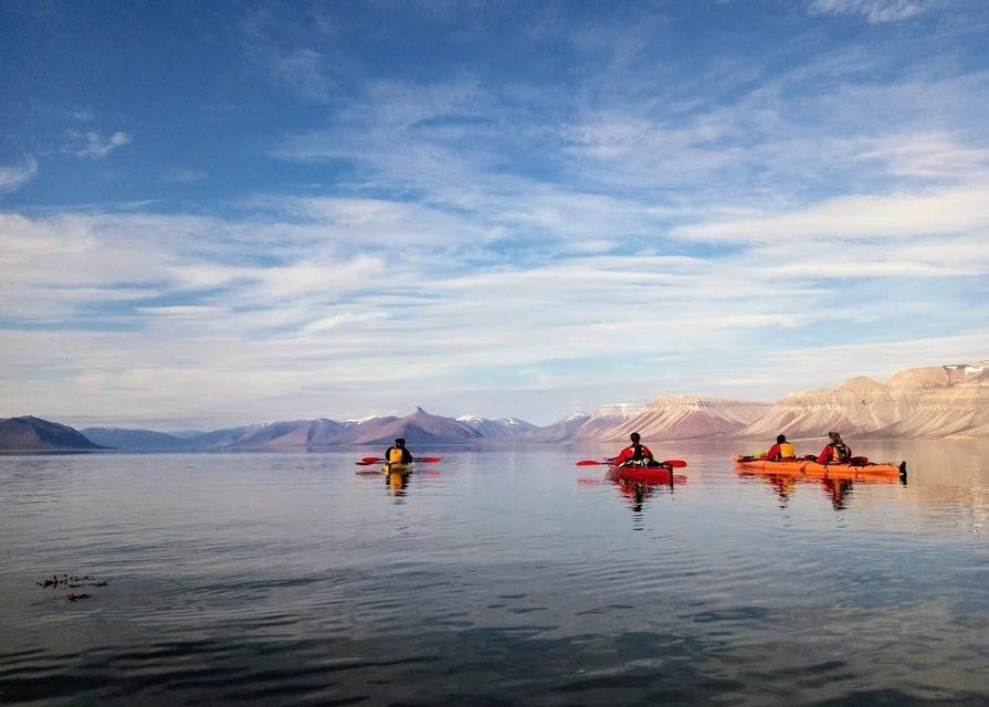 Un viaggio di gruppo WeRoad in kayak su un lago calmo di fronte a montagne innevate sotto un cielo parzialmente nuvoloso.