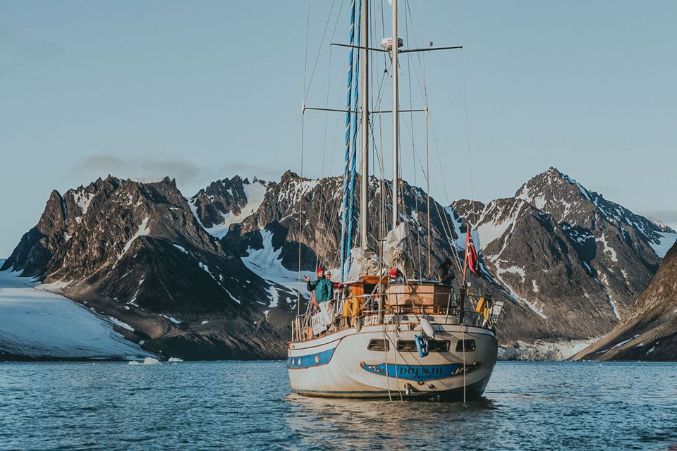Un viaggio di gruppo WeRoad in barca a vela naviga acque calme di fronte a imponenti montagne e ghiacciai innevati.