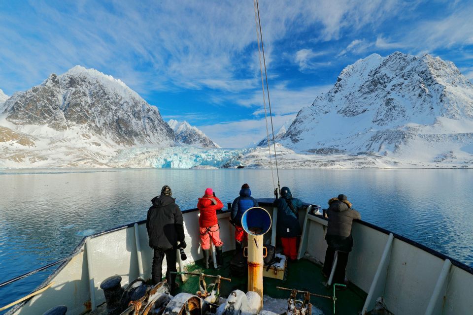 Un viaggio di gruppo WeRoad a prua di una barca osserva un grande ghiacciaio tra montagne innevate.