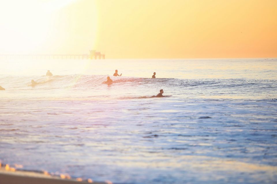 Viaggio di gruppo WeRoad: surfisti sulle tavole nell'oceano, sagome contro un tramonto dorato e un molo sullo sfondo.