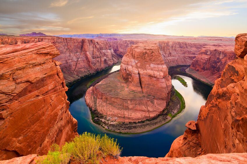 Una vista grandangolare di un fiume che serpeggia attorno a una massiccia formazione rocciosa rossa all'interno di un profondo canyon al tramonto.