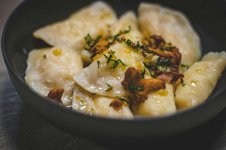 Nahaufnahme von Pierogi-Knödeln in einer dunklen Schale, garniert mit gebratenen Pilzen und frischen Kräutern.