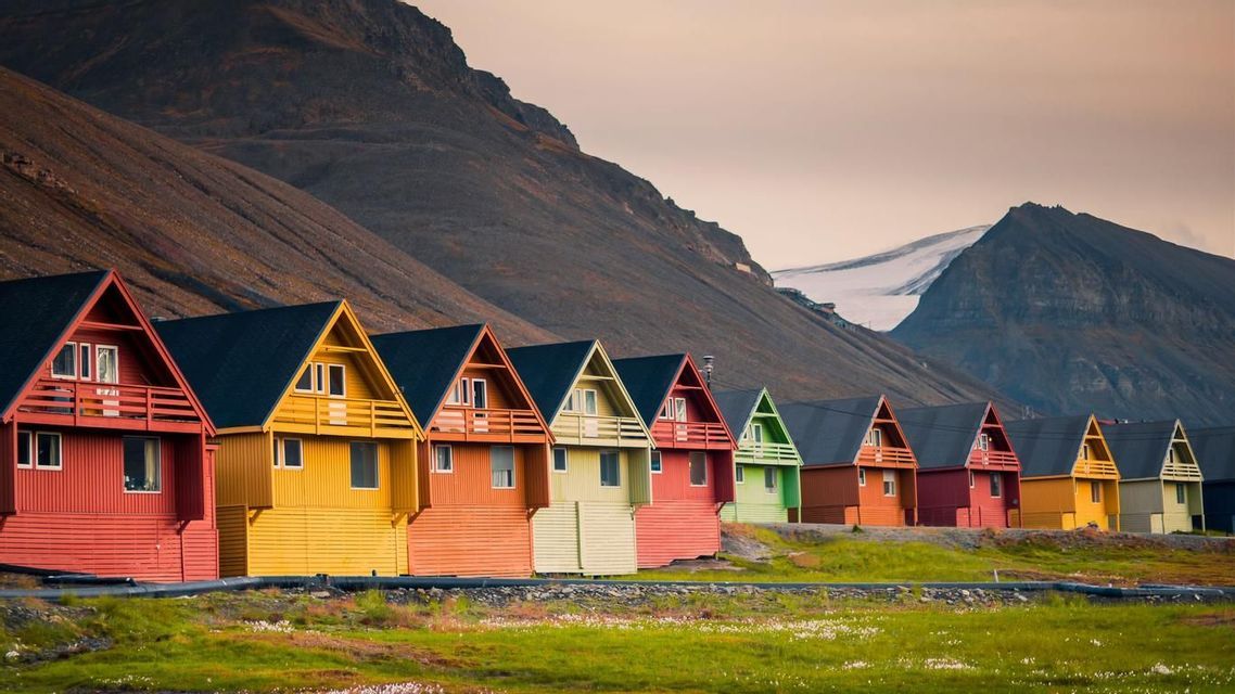 Una fila di casette colorate a tenda si trova su un prato verde, ai piedi di una montagna rocciosa con un ghiacciaio.