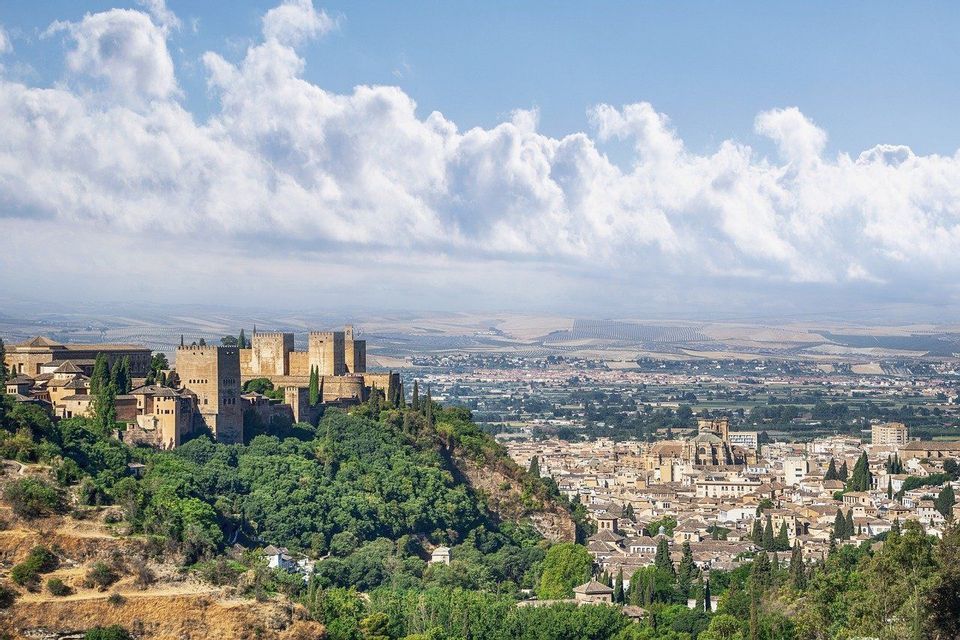 Una fortaleza histórica en una exuberante colina verde domina una ciudad en expansión y llanuras distantes bajo un cielo nublado.