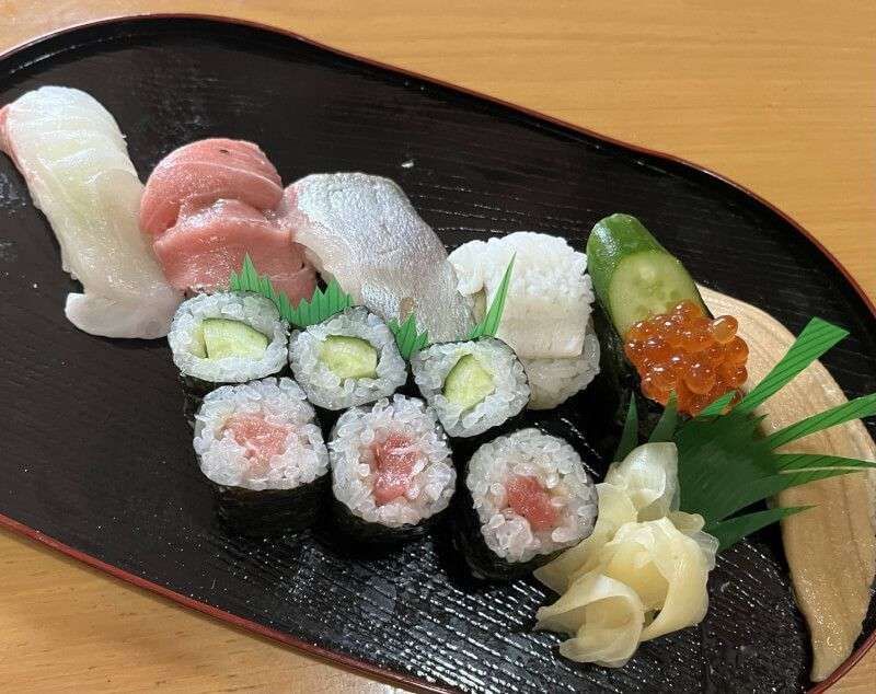 Un assortimento di sushi, inclusi nigiri, maki al tonno e maki al cetriolo, presentato su un vassoio nero con zenzero marinato.