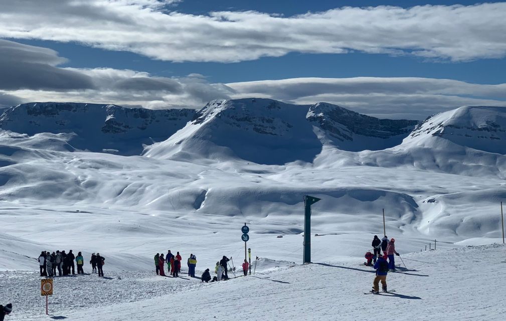 Un gruppo WeRoad si riunisce su una pista da sci innevata, con vaste montagne coperte di neve che si estendono all'orizzonte.