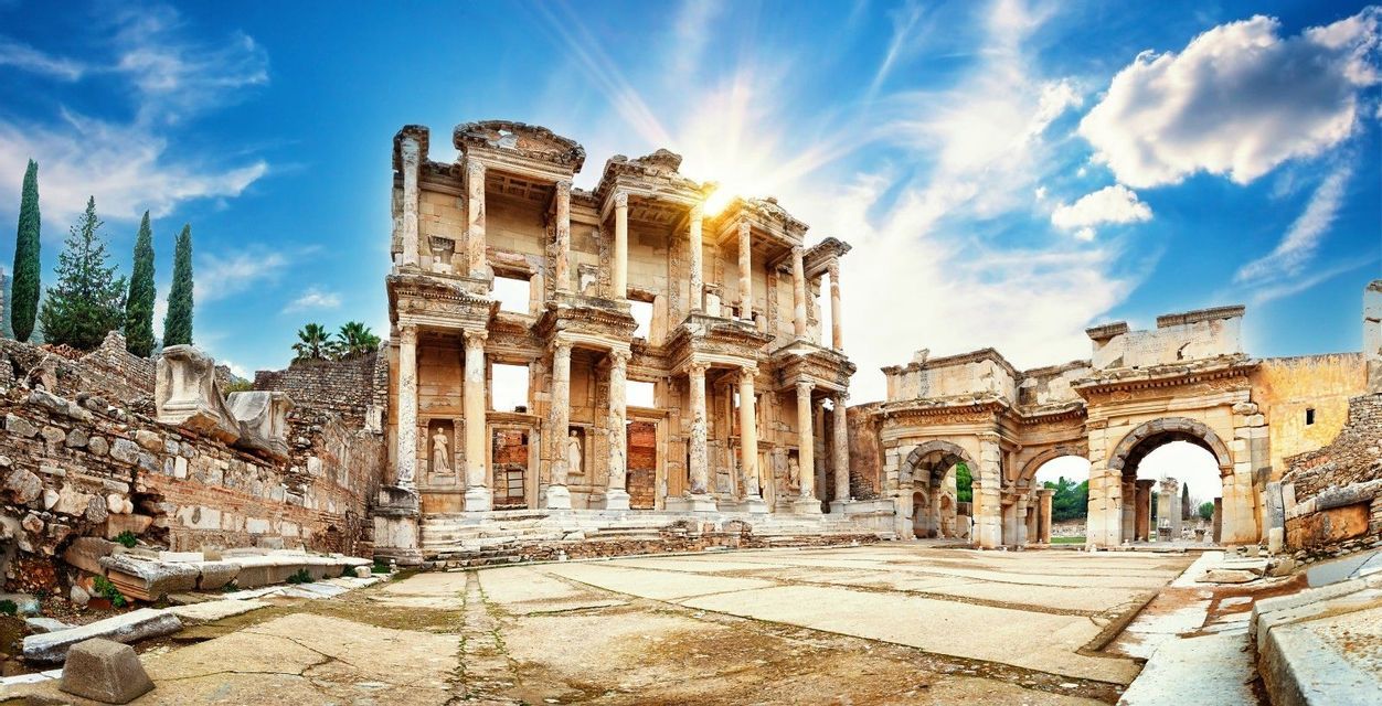 Il sole splende luminoso sulle antiche rovine di un grande edificio con colonne e archi in un cortile in pietra.