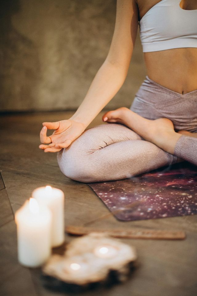 Una persona in posizione yoga del loto medita su un tappetino a stampa galassia con candele accese in primo piano.