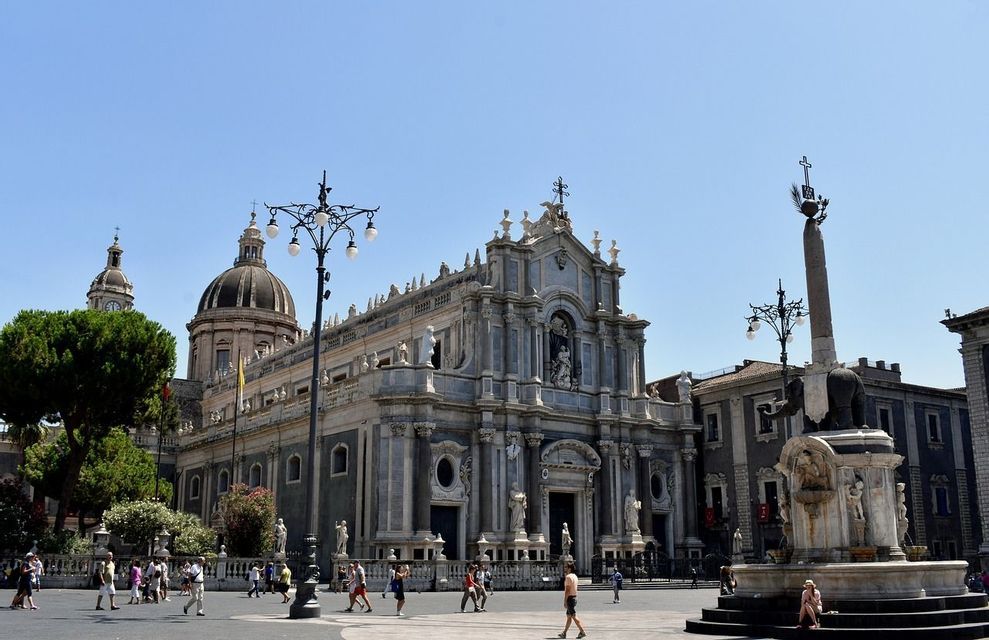 Una cattedrale barocca con una cupola e una fontana con una statua di elefante si ergono in una piazza storica in una giornata di sole.