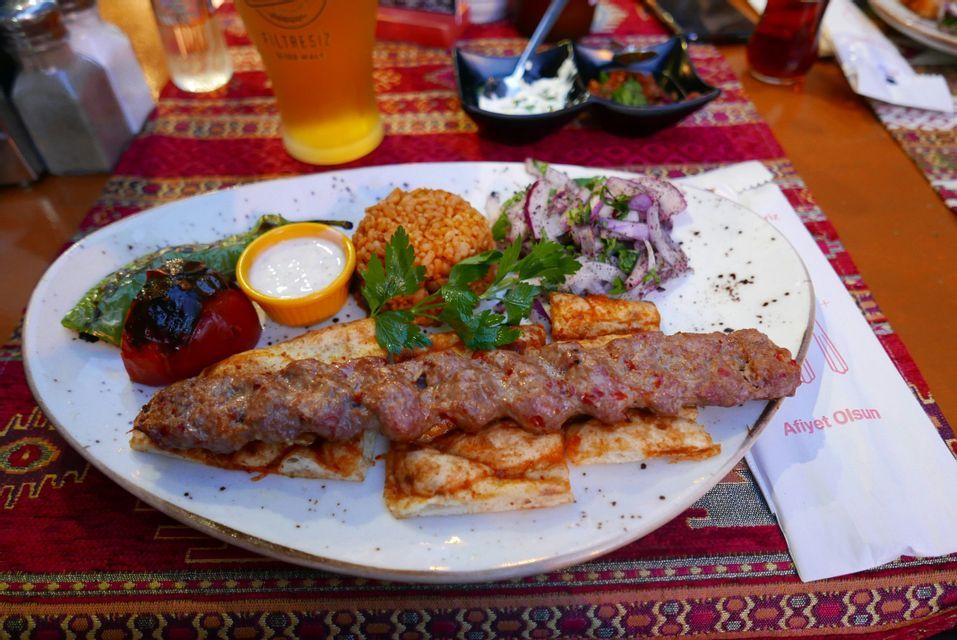 Un plato de kebab turco, con carne a la parrilla sobre pan plano, servido con bulgur, ensalada de cebolla, verduras asadas y salsa.