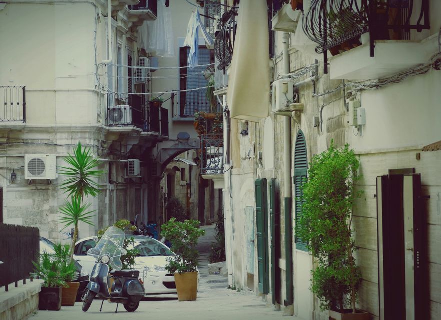 Uno scooter è parcheggiato in un vicolo stretto tra vecchi edifici in pietra con il bucato appeso ai fili sopra.
