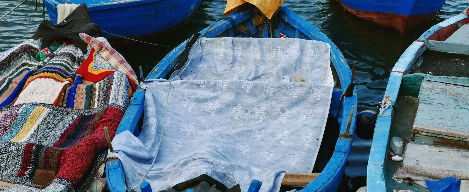 Scatto dall'alto di diverse barche blu rustiche ormeggiate insieme, una riempita con una coperta patchwork colorata.