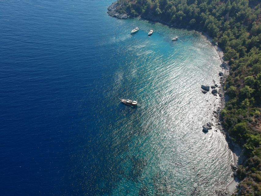 Una vista aerea di diverse barche ancorate in una baia turchese accanto a una costa alberata.