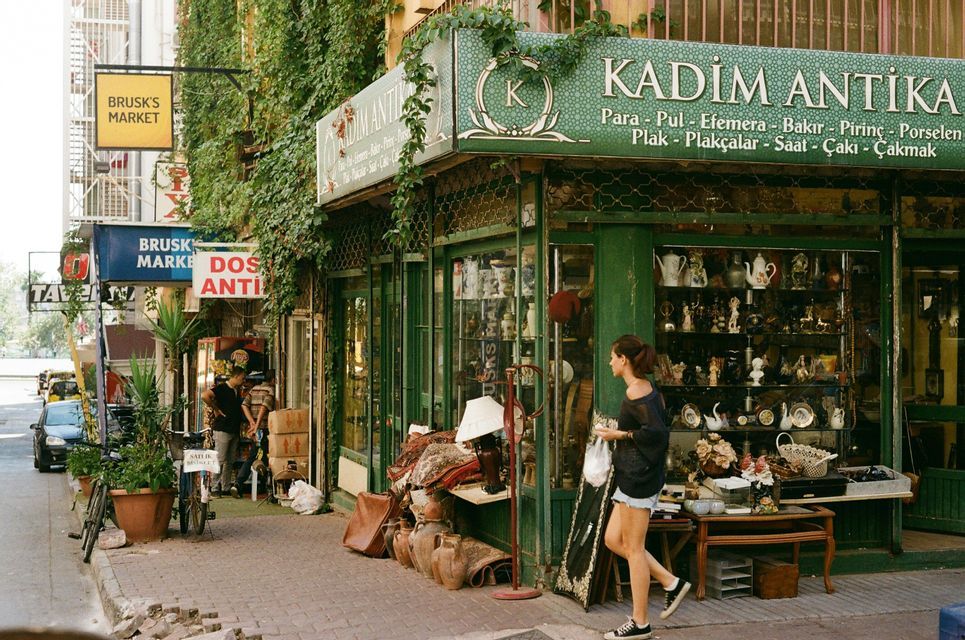 Una donna passa davanti a un negozio di antiquariato su una strada cittadina, con vari oggetti esposti sul marciapiede.