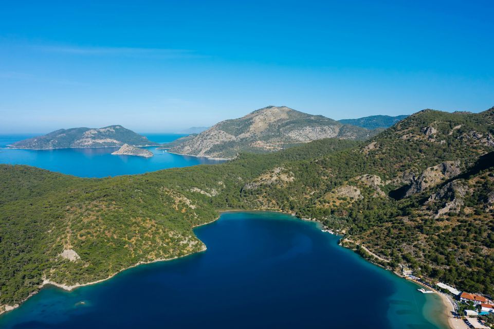 Veduta aerea di una profonda baia blu, circondata da verdi colline e isole alberate sotto un cielo limpido.