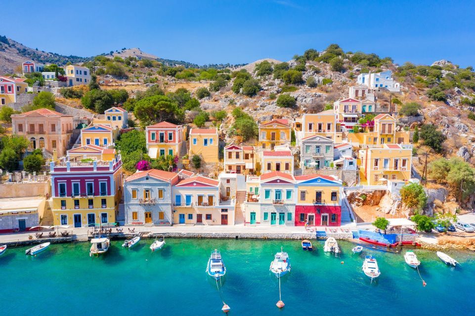 Edifici colorati fiancheggiano un porto in una giornata di sole, con barche ormeggiate nel mare limpido e turchese.