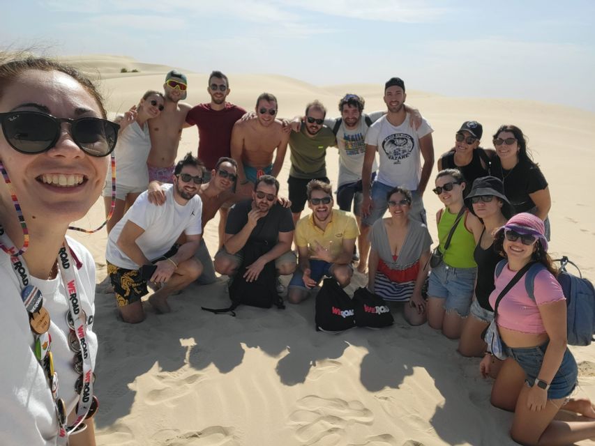 Un grupo de viaje de WeRoad sonriente posa para una foto grupal en una duna de arena soleada.