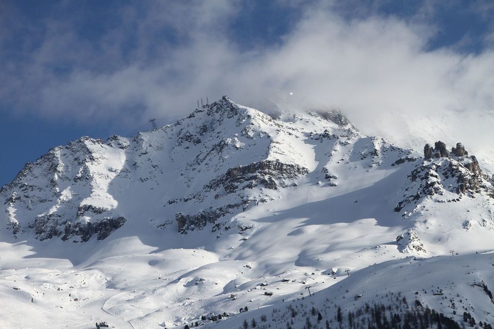 Una montagna innevata con impianti di risalita sulla sua cima e sulle piste, sotto un cielo blu con nuvole bianche.