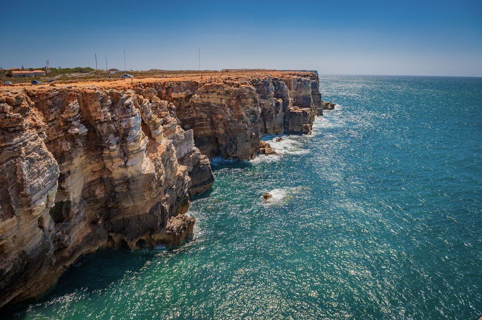 Des falaises rocheuses superposées s'étendent le long d'un océan d'un bleu profond sous un ciel clair et ensoleillé.