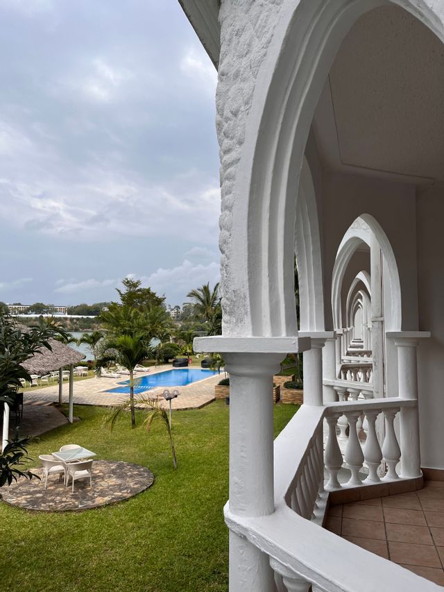 Una vista dal balcone di un resort attraverso una serie di archi bianchi, che si affaccia su un giardino con piscina.