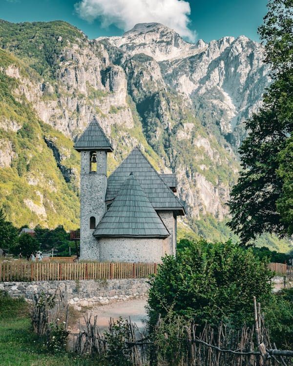 Una storica chiesa in pietra con tetto in ardesia e campanile si trova in una valle ai piedi di imponenti montagne aspre.