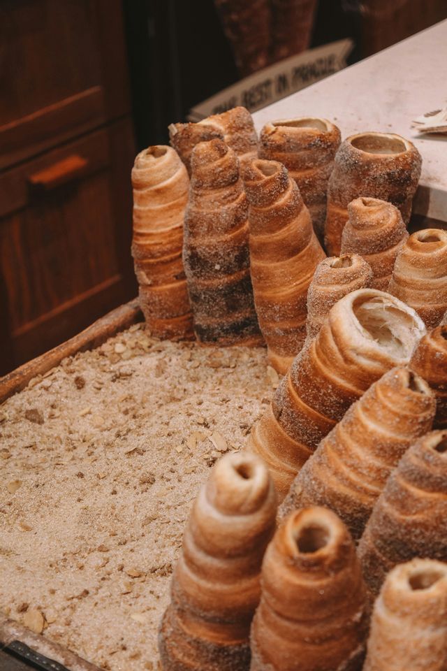 Primo piano di diversi dolci conici, Trdelník, ricoperti di zucchero e disposti verticalmente in un vassoio espositore.