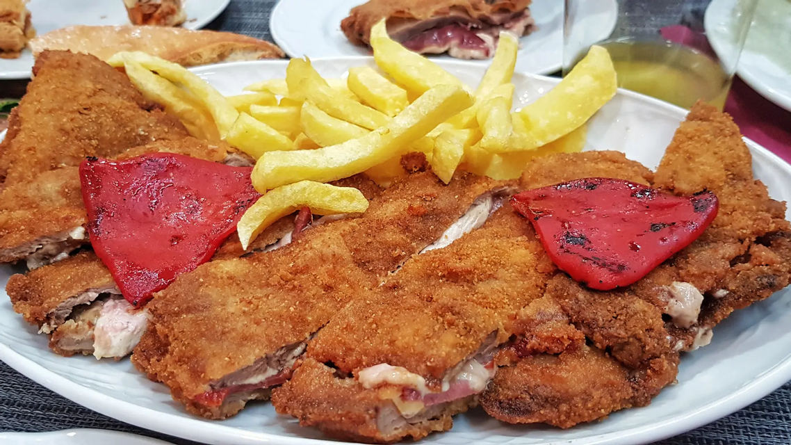 Gran cachopo rebozado y loncheado, relleno de jamón y queso, acompañado de patatas fritas y pimientos rojos asados.