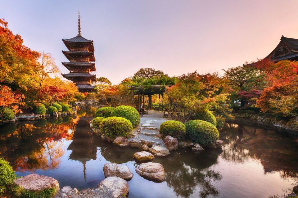 Una tradizionale pagoda giapponese si specchia in un placido stagno, in un giardino ricco di colorati alberi autunnali, al tramonto.