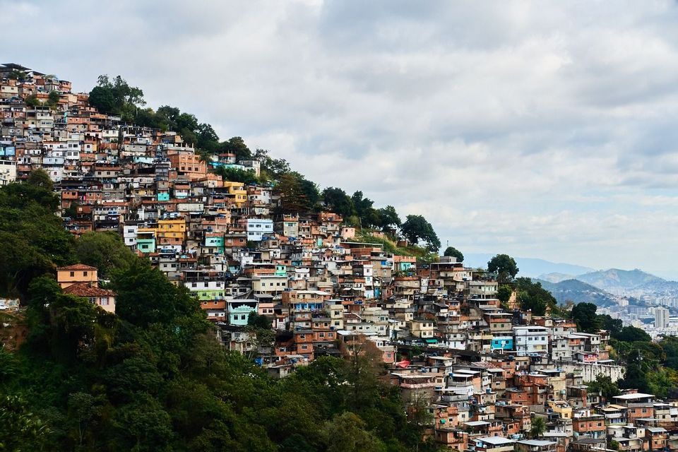 Un ensemble dense de bâtiments colorés s'étend sur une colline luxuriante, sous un ciel nuageux.