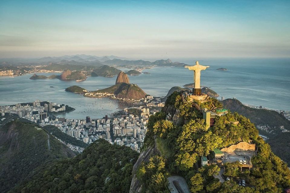 Eine Luftaufnahme der Christus-Erlöser-Statue auf einem Berggipfel, die eine Küstenstadt und eine Bucht mit Inseln überblickt.