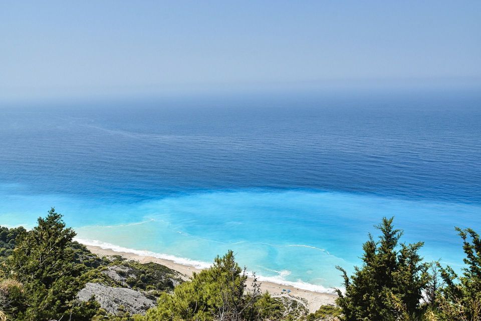 Una veduta dall'alto su alberi verdi mostra una spiaggia sabbiosa con fasce di acqua turchese e blu intenso che si estendono fino all'orizzonte.
