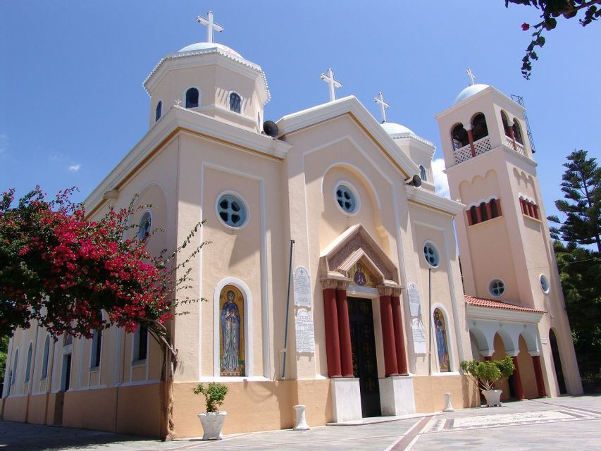 Una chiesa ortodossa color crema, con diverse cupole e un campanile, sorge in un cortile sotto un cielo azzurro e limpido.