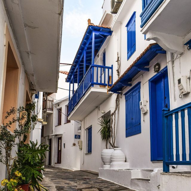 Uno stretto vicolo acciottolato si snoda tra edifici imbiancati con balconi, porte e persiane di un blu brillante.
