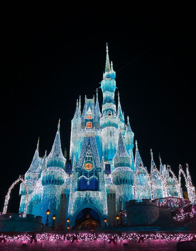 Un château féerique aux nombreuses flèches, entièrement illuminé de lumières bleues et blanches éclatantes se détachant sur le ciel nocturne sombre.