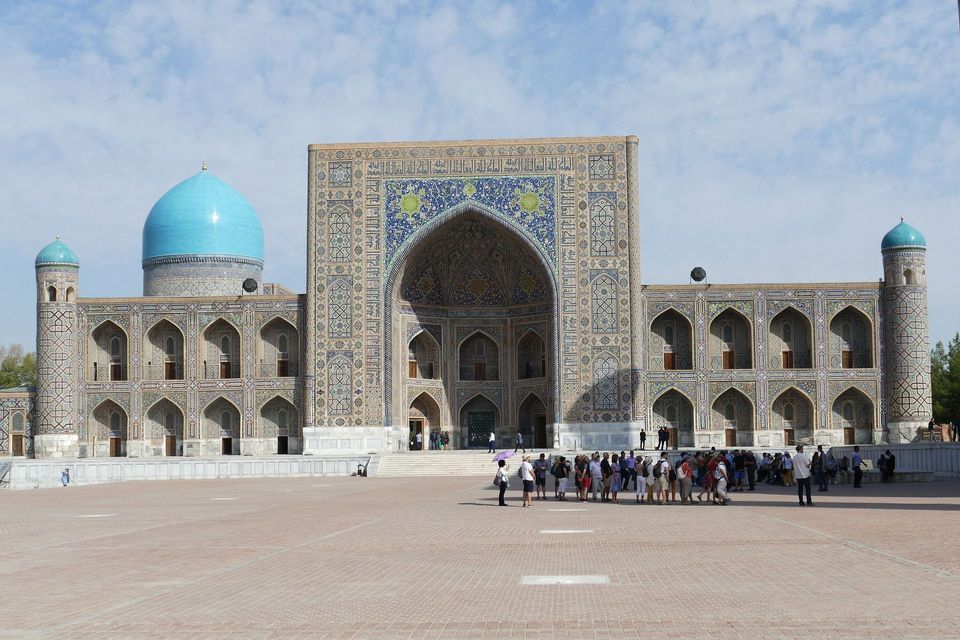 Un gruppo WeRoad è in una grande piazza, ammirando un edificio storico con intricate maioliche blu e una grande cupola.