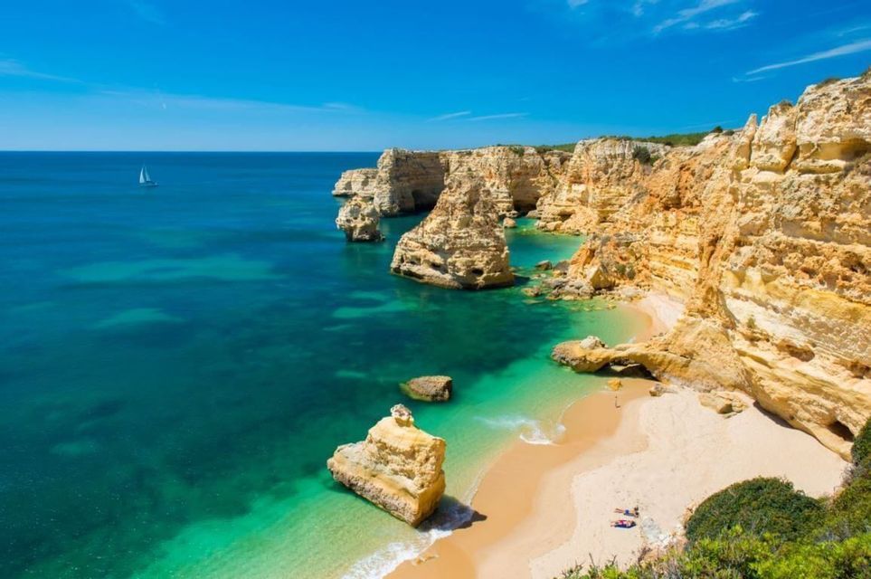 Aerial view of a secluded cove with golden cliffs, a sandy beach, and turquoise water under a clear blue sky.