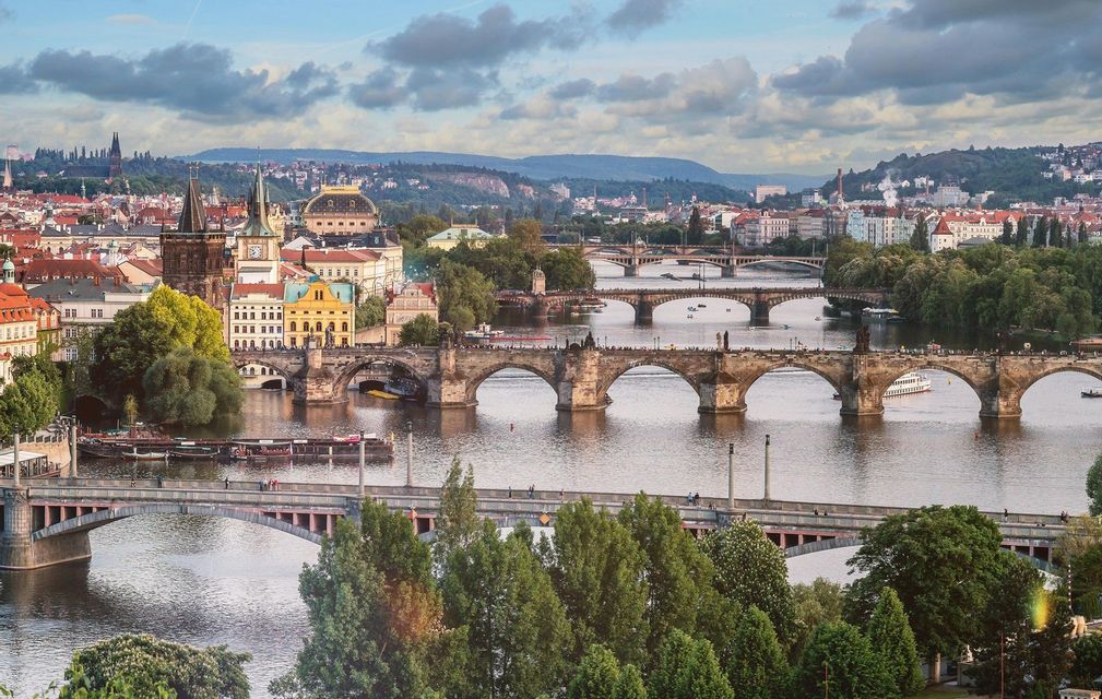 Una vista diurna di più ponti ad arco in pietra che attraversano un ampio fiume che scorre attraverso una città storica con colline sullo sfondo.