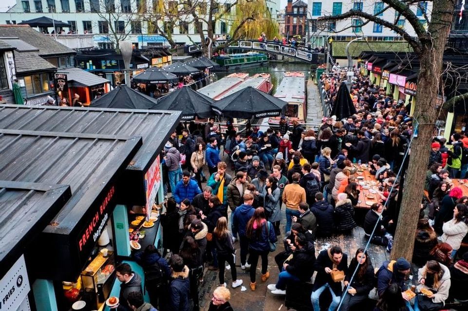 Una veduta dall'alto di una grande folla a un mercato alimentare all'aperto con bancarelle e tavoli vicino a un canale.