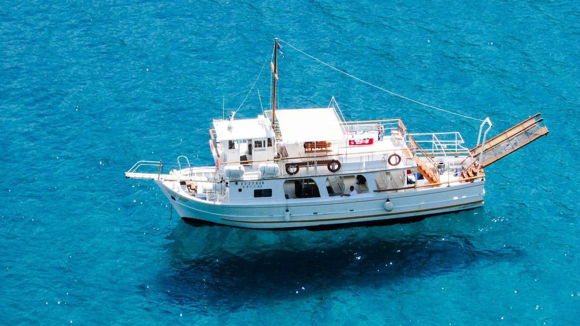 Veduta aerea di una barca bianca che galleggia in acqua limpida e turchese, con l'ombra visibile sotto.
