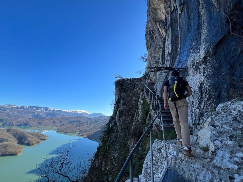 Un viaggio di gruppo WeRoad: escursione su una ripida scalinata metallica a strapiombo su un lago e montagne innevate.