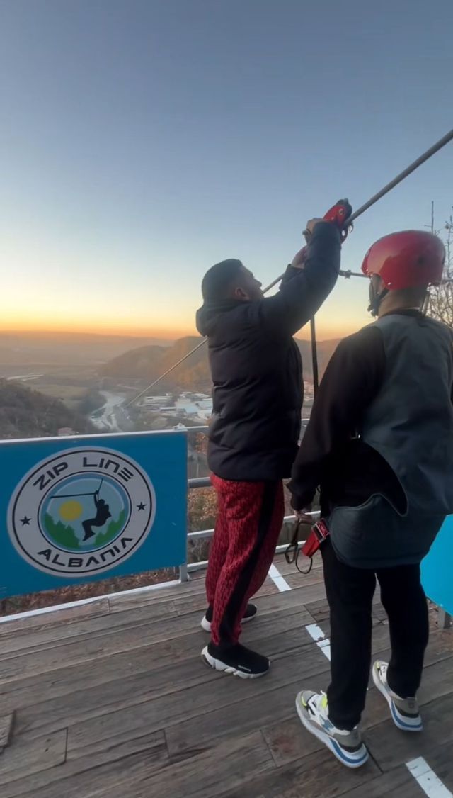 Due persone di un gruppo WeRoad si preparano per una discesa in zipline da una piattaforma di legno, con vista su una valle al tramonto.