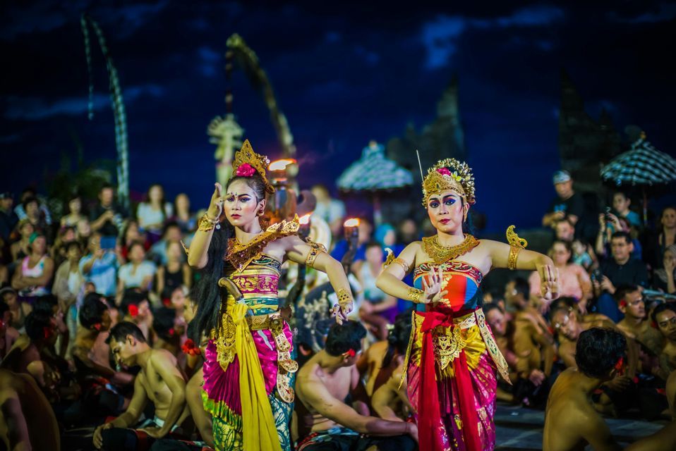 Due donne in elaborati costumi tradizionali e copricapi eseguono una danza culturale per un pubblico di notte.