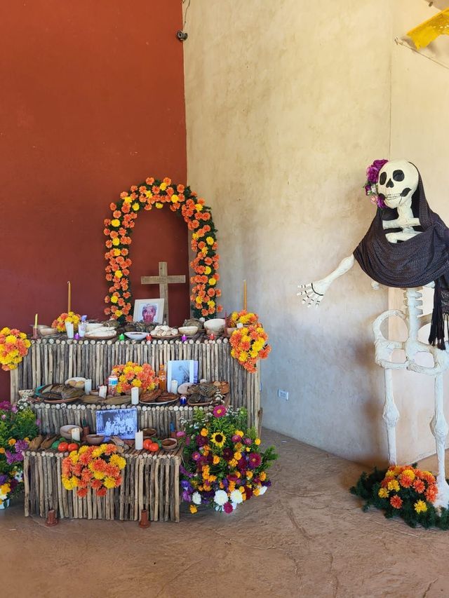 Un tradizionale altare del Giorno dei Morti, decorato con calendule, cibo e foto, si trova accanto a una grande figura di scheletro.