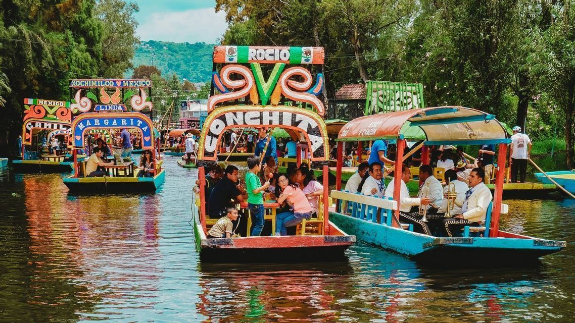 Un viaggio di gruppo WeRoad a bordo di colorate e decorate trajinera su un canale, con musicisti mariachi che suonano da una barca vicina.