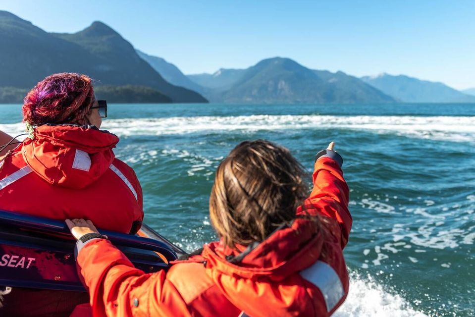 Deux personnes d'un voyage en groupe WeRoad, vêtues de vestes rouges, sur un bateau, l'une d'elles pointant du doigt des montagnes lointaines.
